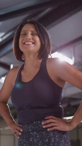 Vertical-Video-Portrait-Of-Smiling-Mature-Woman-Wearing-Fitness-Clothing-Standing-In-Gym-Ready-To-Exercise-3